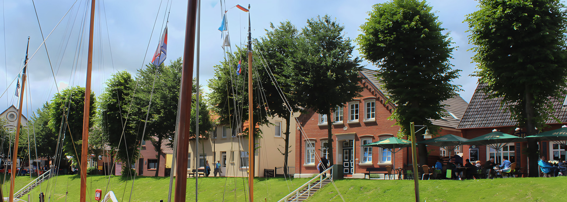 Haus am Museumshafen hinter Segelschiffen in Carolinensiel – Ferienwohnungen direkt am Hafen der Nordsee