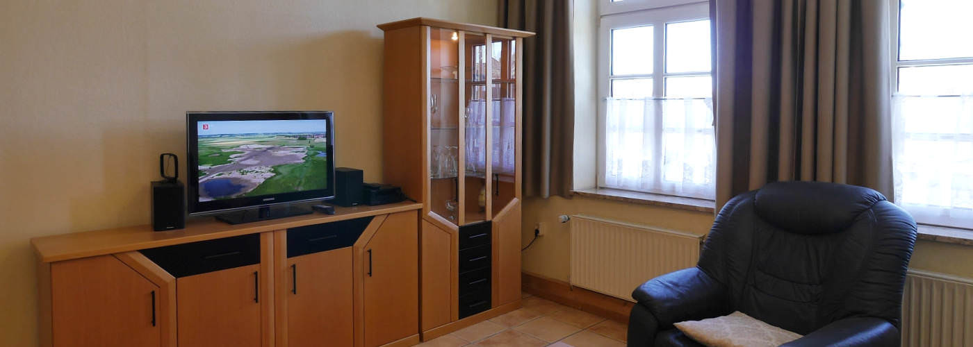 Gemütliches Wohnzimmer der Ferienwohnung Kutter in Carolinensiel mit Ledersessel, Fernseher und Holzmöbeln