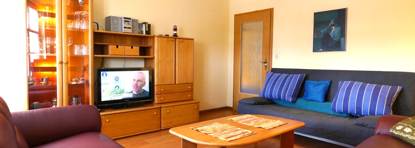 Wohnzimmer der Ferienwohnung Schoner am Museumshafen von Carolinensiel mit blauen Sofas und Holzmöbeln