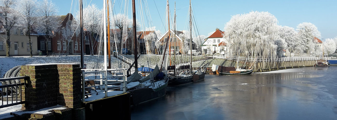 Verschneite Traditionssegler und Häuser am winterlichen Museumshafen von Carolinensiel